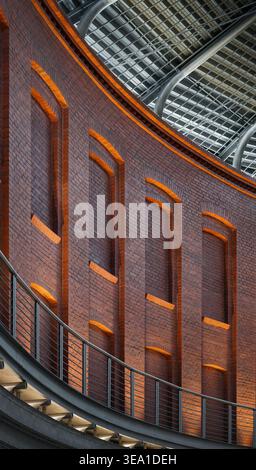 Brick wall with arched niches under steel roof. A curved red brick facade featuring blind arched windows and modern industrial details. Stock Photo