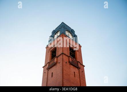 Red brick clock tower of Stary Browar against clear blue sky. A low-angle symmetric view of the red brick tower with dark metal top with classic clock Stock Photo