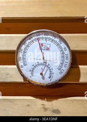 Vintage analog thermometer mounted on wooden slats. Red needle indicates temperature in degrees Celsius. Circular dial shows both temperature and humi Stock Photo