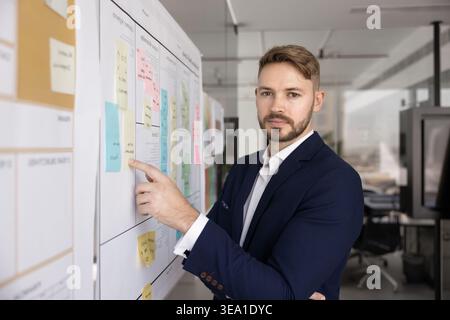Businessman pointing to sticky note while looks at camera Stock Photo