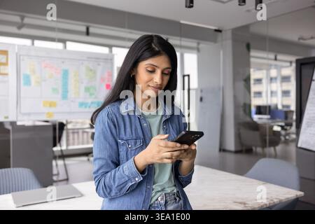 Young professional woman using smartphone while standing in modern office Stock Photo