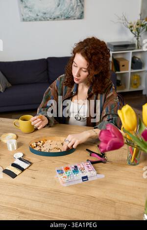 A beautiful woman passionately crafts handmade items while sipping tea in her cozy space. Stock Photo
