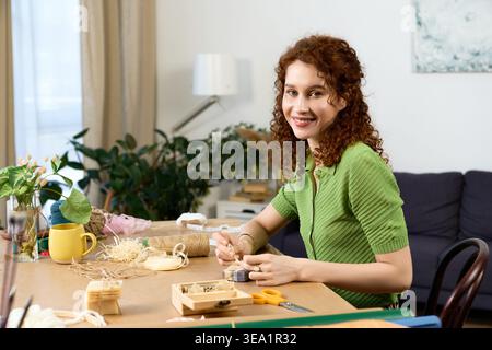 A talented woman enjoys her creative hobby, surrounded by colorful materials in a cozy room. Stock Photo