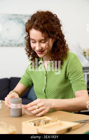 A beautiful woman enjoys creating handmade crafts in her tranquil living room, radiating happiness. Stock Photo