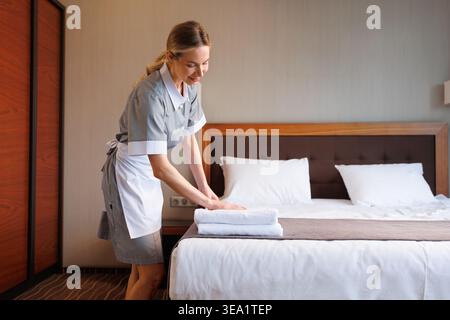 Housekeeper carefully arranging folded towels on hotel bed in guest room Stock Photo