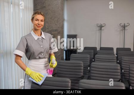 Professional janitor standing with cleaning supplies in office conference room Stock Photo
