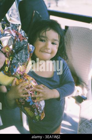 analog film photo of girl holding broken chocolate Easter egg at home. Messy eating and childhood indulgence concept. Copy space for text Stock Photo