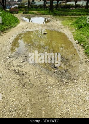 Muddy water puddle on a rough gravel country road after rain. Stock Photo