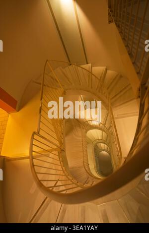Spiral staircase viewed from above in a Sicilian building, featuring warm golden lighting and geometric metal railings creating a mesmerizing downward Stock Photo