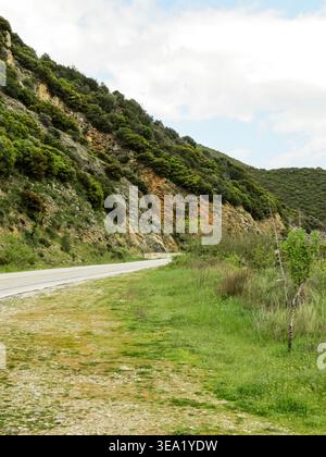 Empty asphalt road winding through green hills and mountain slopes under cloudy sky. Stock Photo