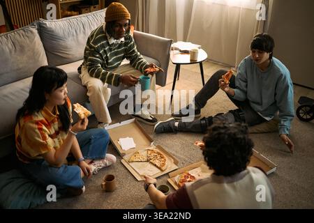 High angle view of diverse teenagers sharing pizza during casual home gathering, socializing and relaxing. Suitable for youth lifestyle, friendship, inclusion, community campaign marketing Stock Photo