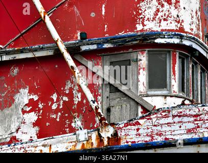 Board bars wooden door on old Fishing Trawler in Oregon.  Red and blue paint is cracked and peeling.  Metal is rusting. Stock Photo