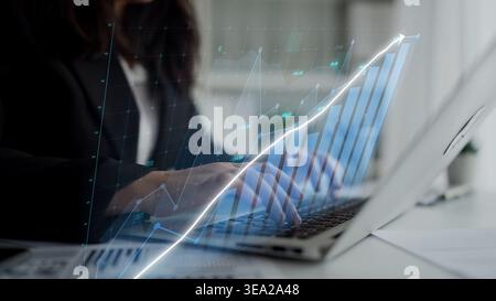 A businesswoman analyzes data on her laptop, with futuristic graphs displayed on the screen. This image captures a modern workspace focused on growth Stock Photo