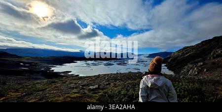 Woman sitting on a cliff and watching the glacier in Iceland Stock Photo