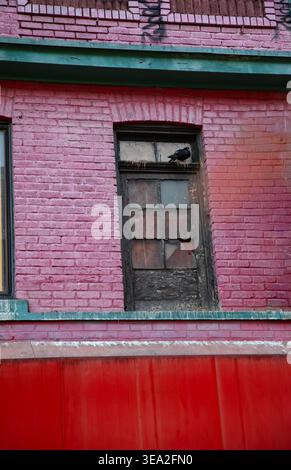 A worn window set in a faded red brick wall with peeling paint and urban texture Stock Photo