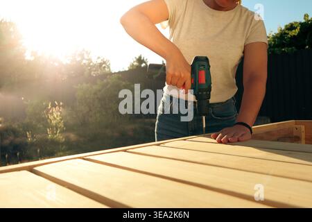 Female carpenter at work using hand drilling machine. Female carpenter building a wooden cabinet with an electric drill Stock Photo