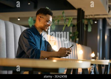 Smiling young businessman texting on smartphone while sitting in office lounge during evening Stock Photo