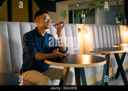 Young businessman talking on speakerphone while sitting in office lounge during evening Stock Photo