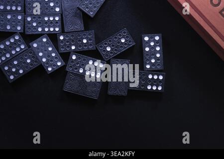 Several scattered domino pieces in the top left corner on a black surface with some facing up and others facing down. Stock Photo