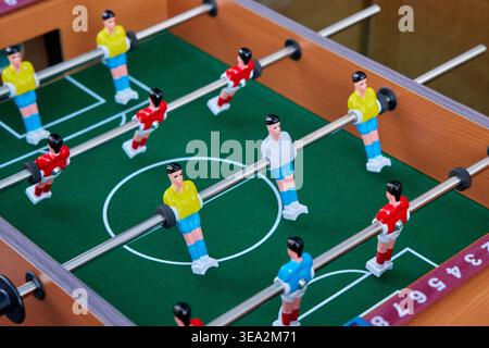 Close-up of a wooden foosball table with red and yellow players on a green field. Indoor table soccer game for leisure and recreation. Stock Photo