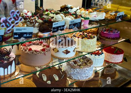 Bakery display case filled with various gourmet cakes, pastries, and tarts. Assorted sweet desserts on glass shelves in a cafe or shop. Stock Photo