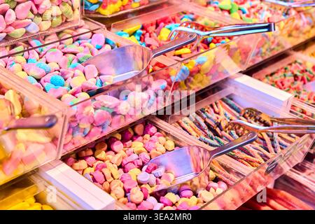 Assorted colorful gummy candies and jelly beans in plastic bins with metal scoops. Variety of sweets in a self-service candy store. Stock Photo