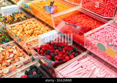 Assorted colorful gummy candies and jelly beans in plastic bins with metal scoops. Variety of sweets in a self-service candy store. Stock Photo