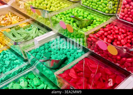 Assorted colorful gummy candies and jelly beans in plastic bins with metal scoops. Variety of sweets in a self-service candy store. Stock Photo