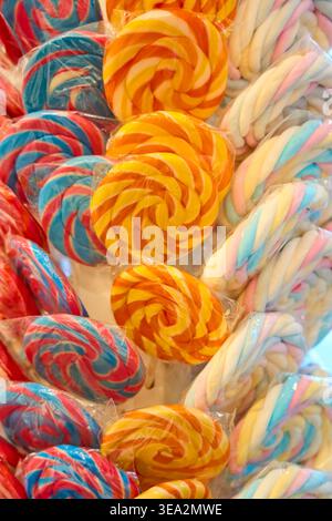 Colorful spiral lollipops in plastic wrappers. Close-up of bright swirl round candies in various colors for sale in a shop. Stock Photo