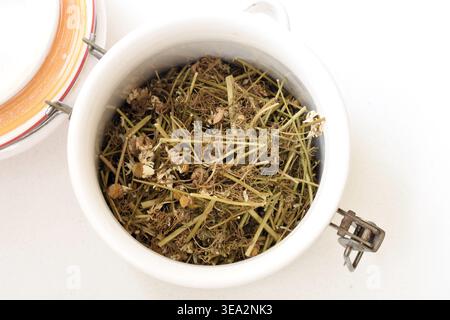 Top view of a container filled with dried chamomile placed on a clean white table. Minimalist composition highlighting natural texture, organic color, Stock Photo