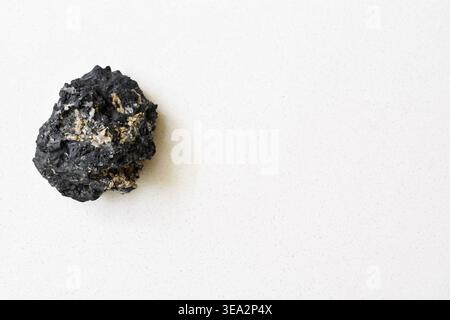 Top view of a black tourmaline crystal placed on a clean white table. Minimalist composition highlighting rough texture, deep color, and natural form. Stock Photo
