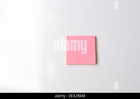 Minimalist image of a pink sticky note attached to a clean wall. Simple composition highlighting color contrast and empty space. Ideal for concepts li Stock Photo