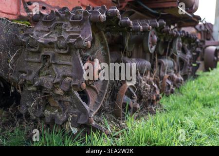 Rusty tractor track detail in grass, weathered crawler machinery texture for agriculture, industrial decay, mechanical engineering, vintage equipment. Stock Photo