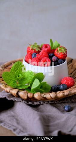 A high angle shot of vibrant raspberries, blueberries, and strawberries in a ceramic bowl. Natural soft lighting highlights the organic textures of th Stock Photo