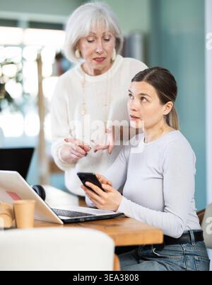 Senior woman boss found female subordinate idling and scrolling phone, mentor shouts at subordinate. Stock Photo