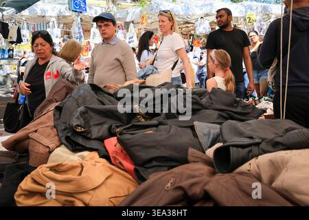 Shoppers looking through leather jackets at a Porta Portese market stall. Rome, Italy - April 19, 2026: A group of shoppers stands around a large pile of second-hand leather jackets in various shades of brown and black. A woman in a grey hoodie gestures toward the merchandise while others look on. In the background, white market umbrellas and various price signs are visible under the bright morning light at the flea market. Rome RM Italy Copyright: xGennaroxLeonardix Stock Photo