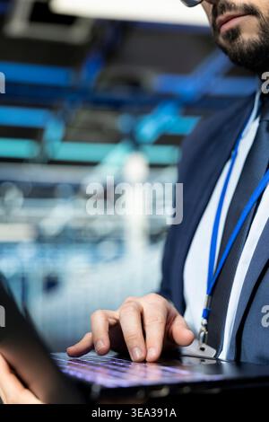 Close up of programmer in data center typing on laptop keyboard, upgrading rigs. IT staff member using notebook in modern server farm to enhance operational effectiveness of hardware Stock Photo