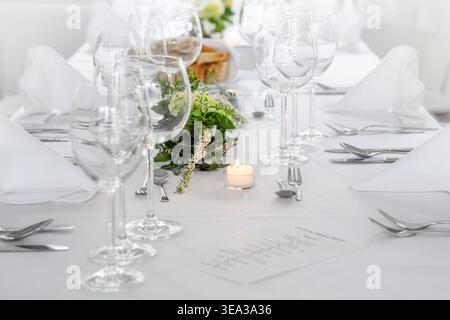 Festively set table for a holiday dinner, with white tablecloths, napkins, glasses, flower decoration, candle and a menu card, Wedding, Christmas, ann Stock Photo