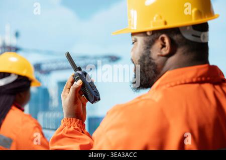 Close up of drilling rig expert speaking in walkie talkie, doing quick response coordination, working in dangerous conditions. Employee listens to coworker talking using handheld radio transceiver Stock Photo