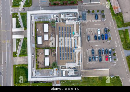 Aerial view of a modern industrial building featuring solar panels on the roof and an adjacent parking lot with several cars in Reggello, Tuscany, Ita Stock Photo
