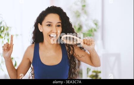 Woman Smiles in Front of a Mirror While Brushing Her Curly Hair and Enjoying Her Time Stock Photo