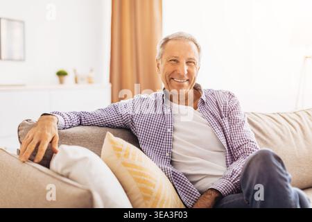Senior Man Relaxing on Couch in Bright Living Room While Smiling at the Camera Stock Photo