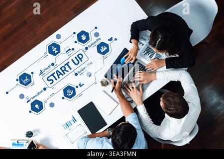 A diverse team collaborates on a startup business plan, utilizing laptops and documents at a modern office table, illustrating innovation and Stock Photo
