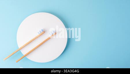 Minimal composition with two bamboo toothbrushes on white circle over blue background with copy space. Top view, flat lay. Stock Photo