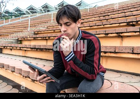 Young man thinking while working on tablet outdoors Stock Photo