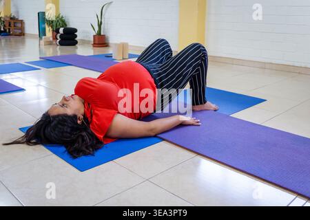 Pregnant woman exercising on a yoga mat, doing postnatal bridge pose Stock Photo