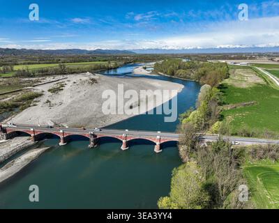 Aerial view of the red brick arched bridge crossing the Po river with a large gravel bank and snow-capped Alps in the background Verrua Savoia, Piedmo Stock Photo
