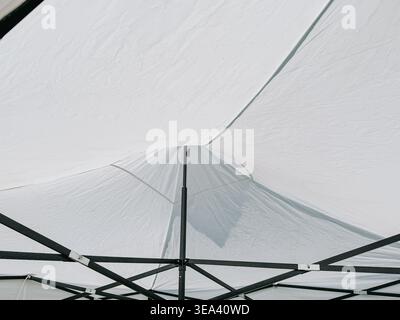 Interior view of a white canopy tent showing taut fabric and black metal support frame. Clean geometric composition ideal for concepts of temporary st Stock Photo