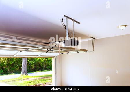 Garage door opener is mounted on ceiling, with door open, allowing to shine in. Stock Photo