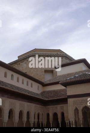 Layered Nasrid tiled rooflines, carved stucco arcade, and octagonal tower against an overcast sky, Court of the Lions, Alhambra Palace, Granada, Spain Stock Photo